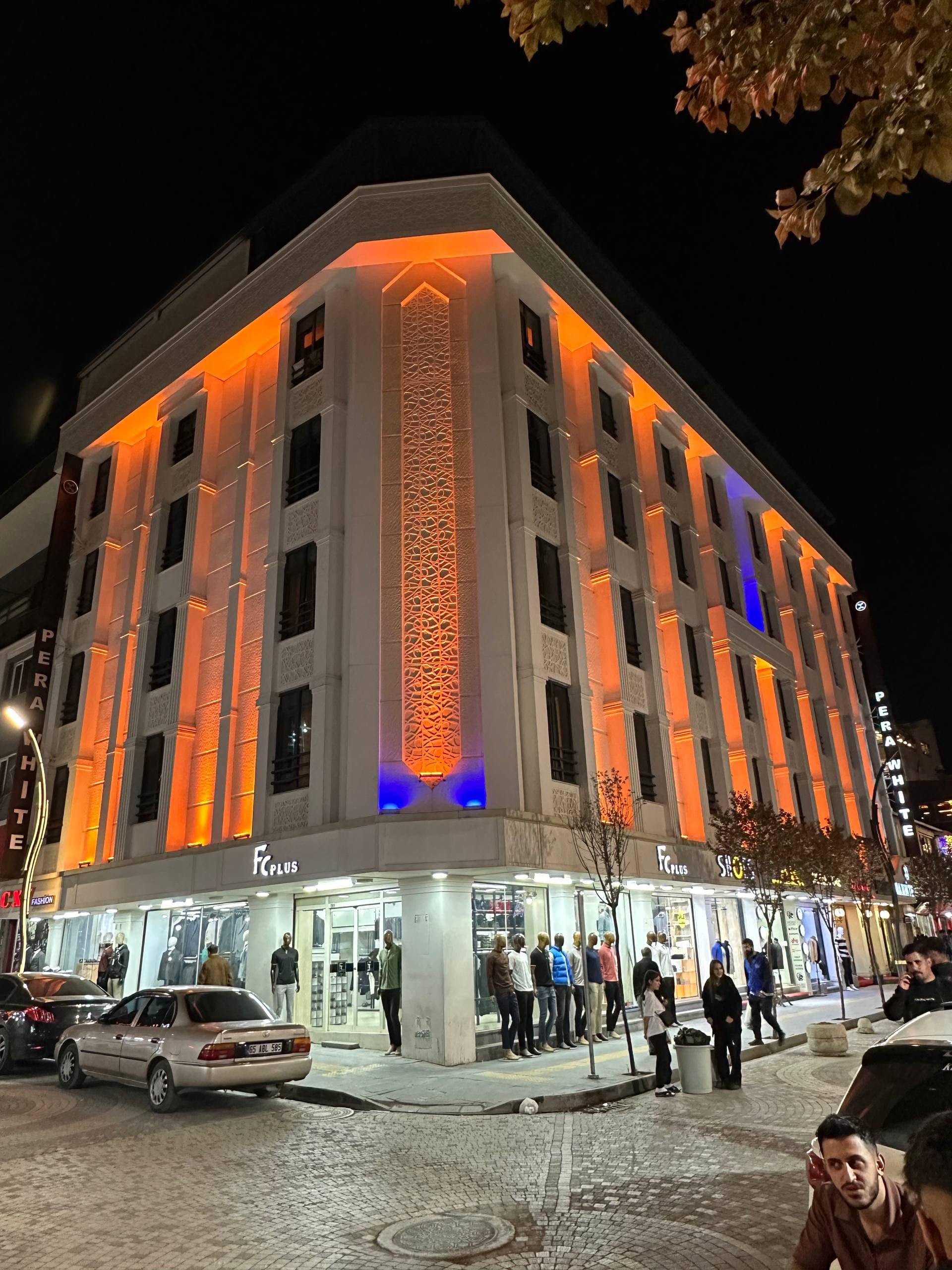 Sıcak portakal ışıklarla aydınlatılmış otel cephesi ve dolu sokak
