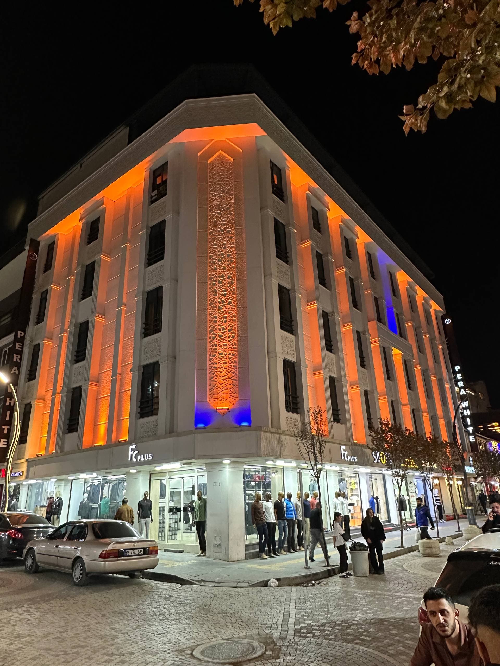 Otel köşesi yakın plan: aydınlatmalı dikey örgü motifi ve giriş katı vitrinleri